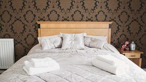 Un lit bien fait, avec une couverture matelassée et des oreillers, une tête de lit en bois et une table de chevet ornée d’un vase et de fleurs.