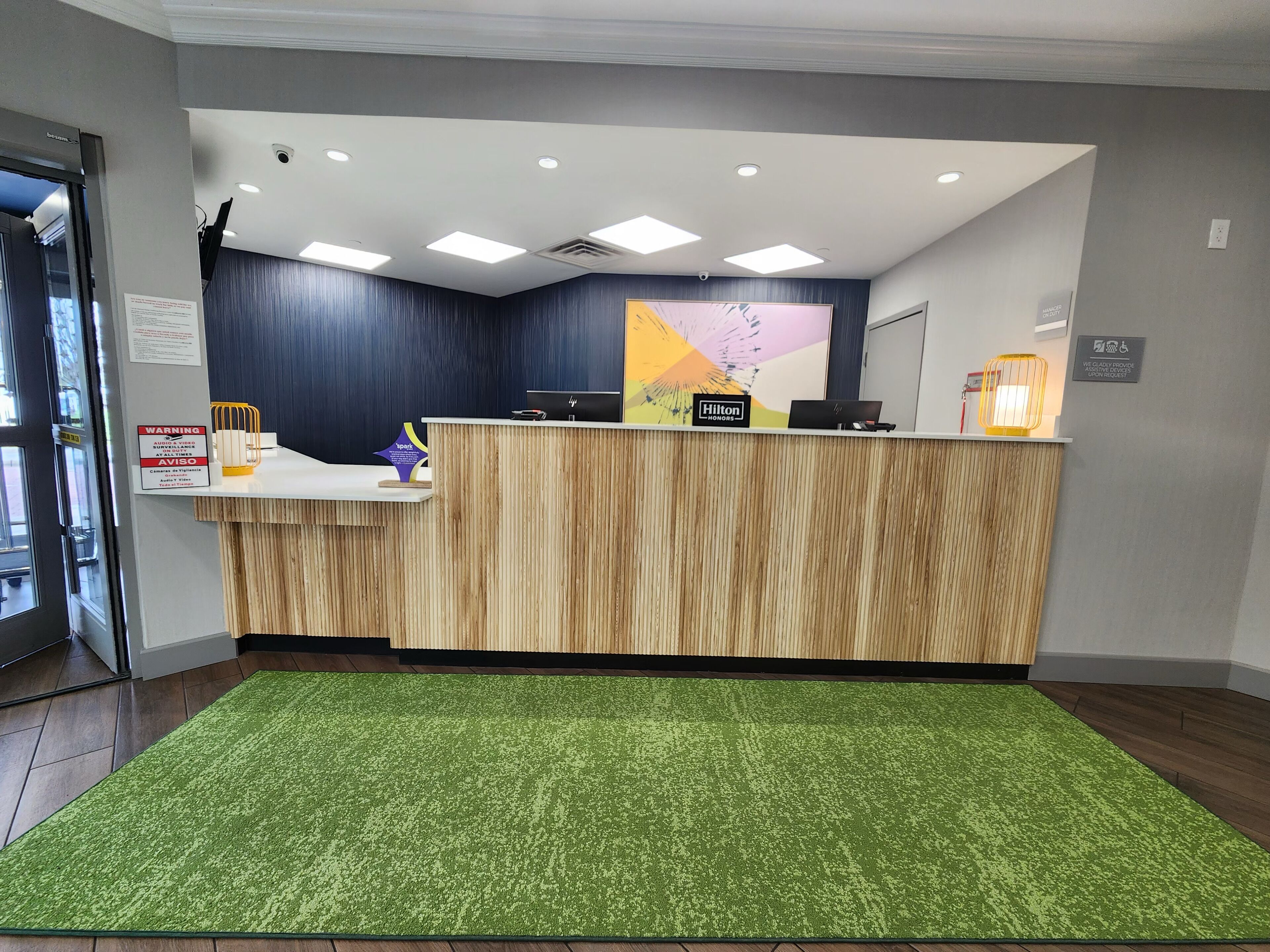 A hotel reception desk with a wooden finish, a green carpet, and a sign indicating it is a Hilton Honors hotel.