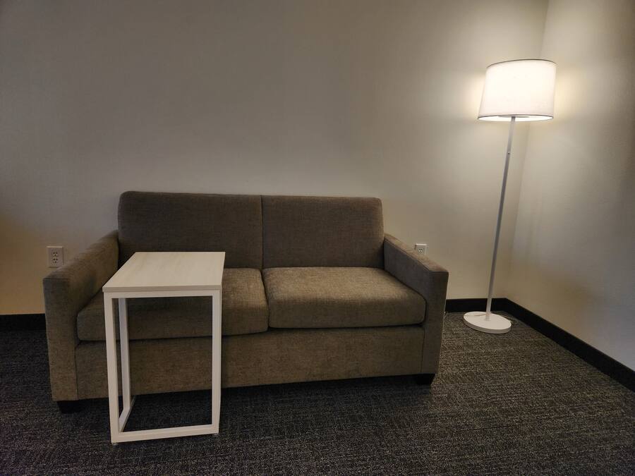 A neutral-toned sofa with a small white side table in front, a floor lamp to the right, and a carpeted floor.