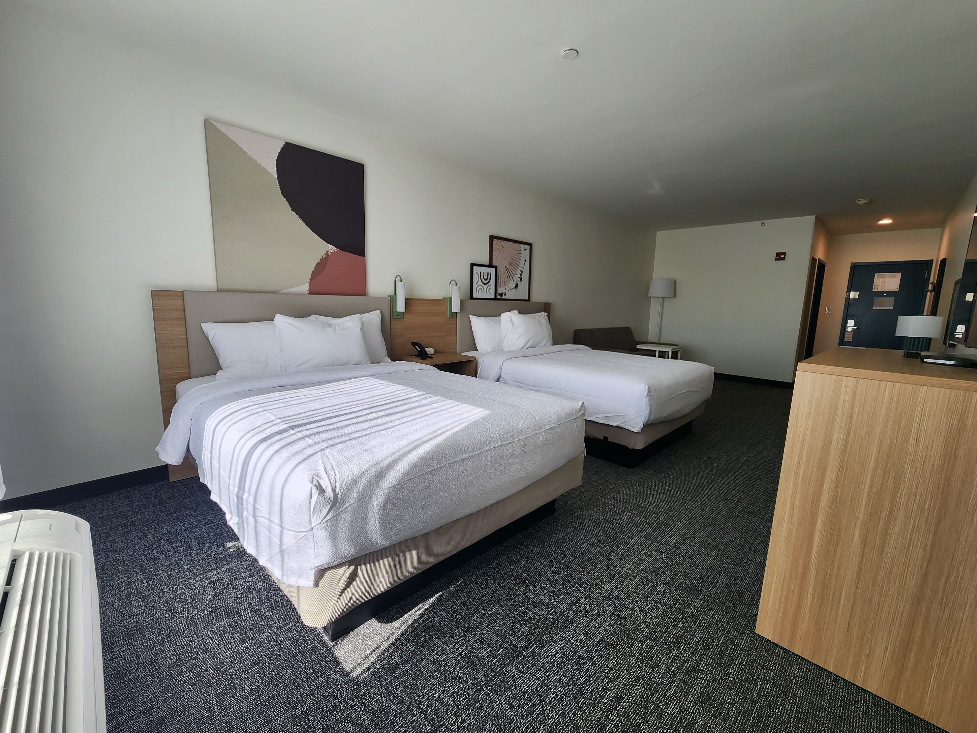 Une chambre d’hôtel avec deux lits, un bureau et un grand tableau abstrait accroché au mur.