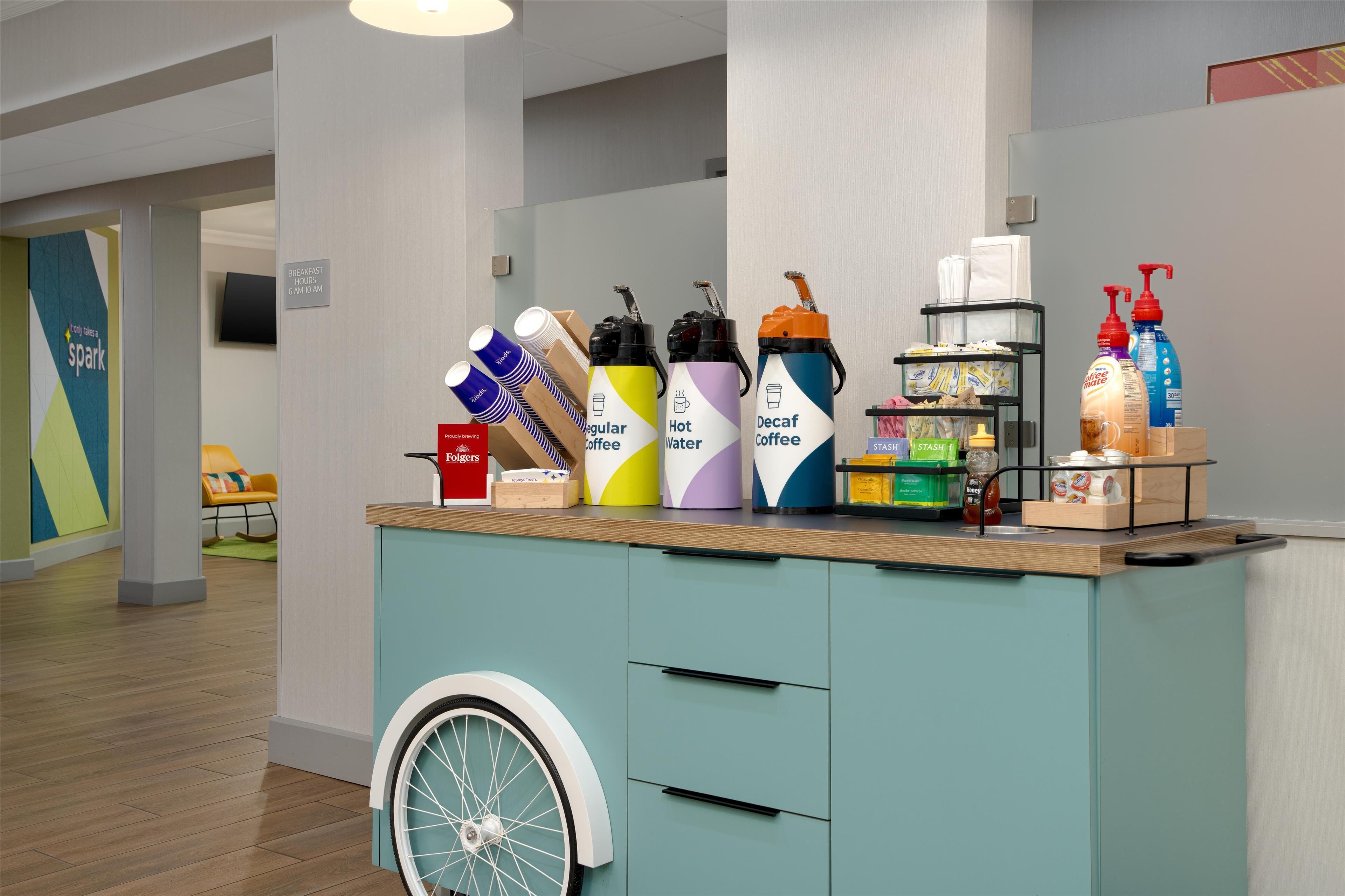Mostrador con varios dispensadores de bebidas, una silla de ruedas y un cartel que indica servicio de desayuno.