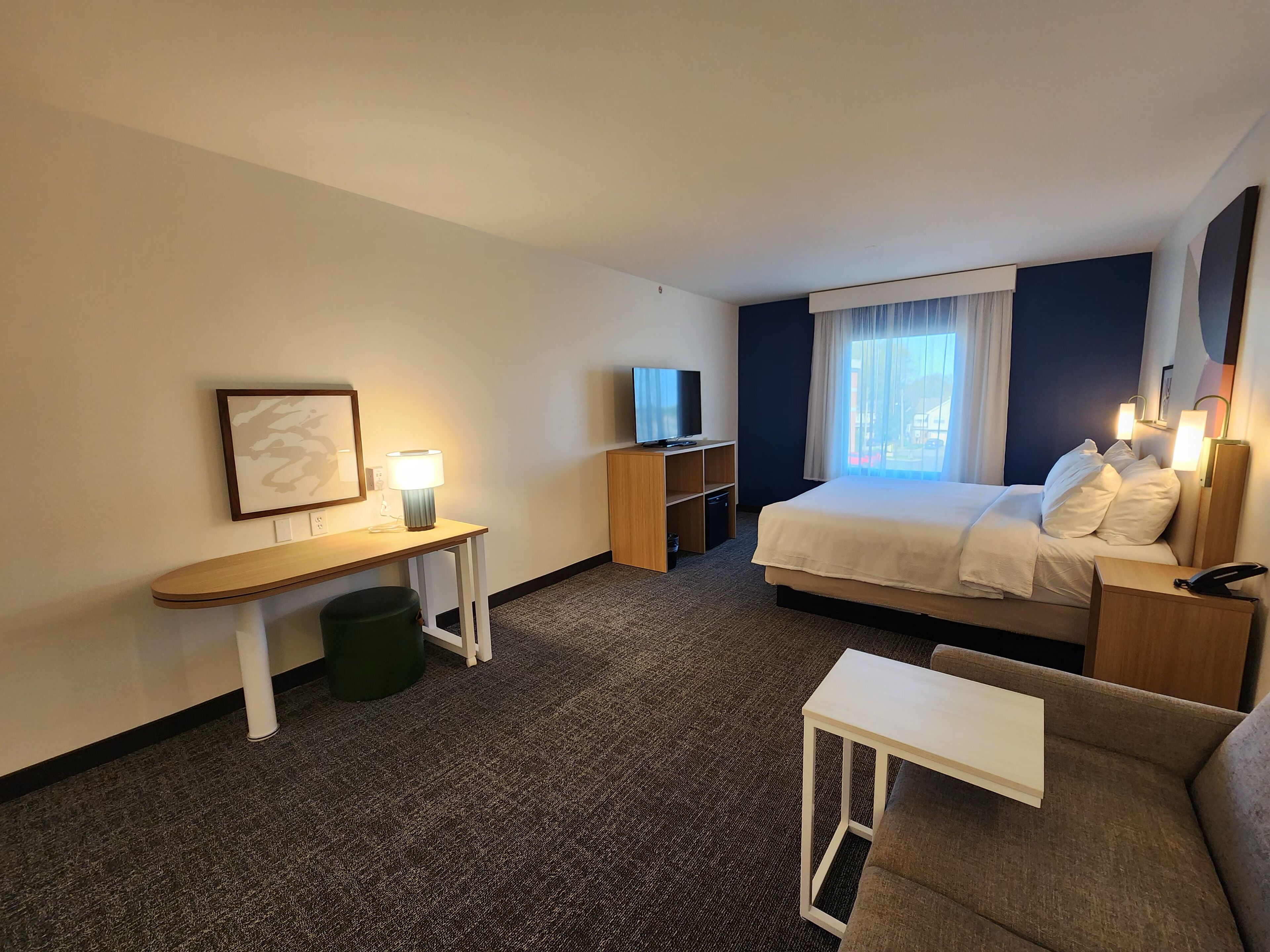 A hotel room with a bed, a desk, a TV, a sofa, and a window with curtains.