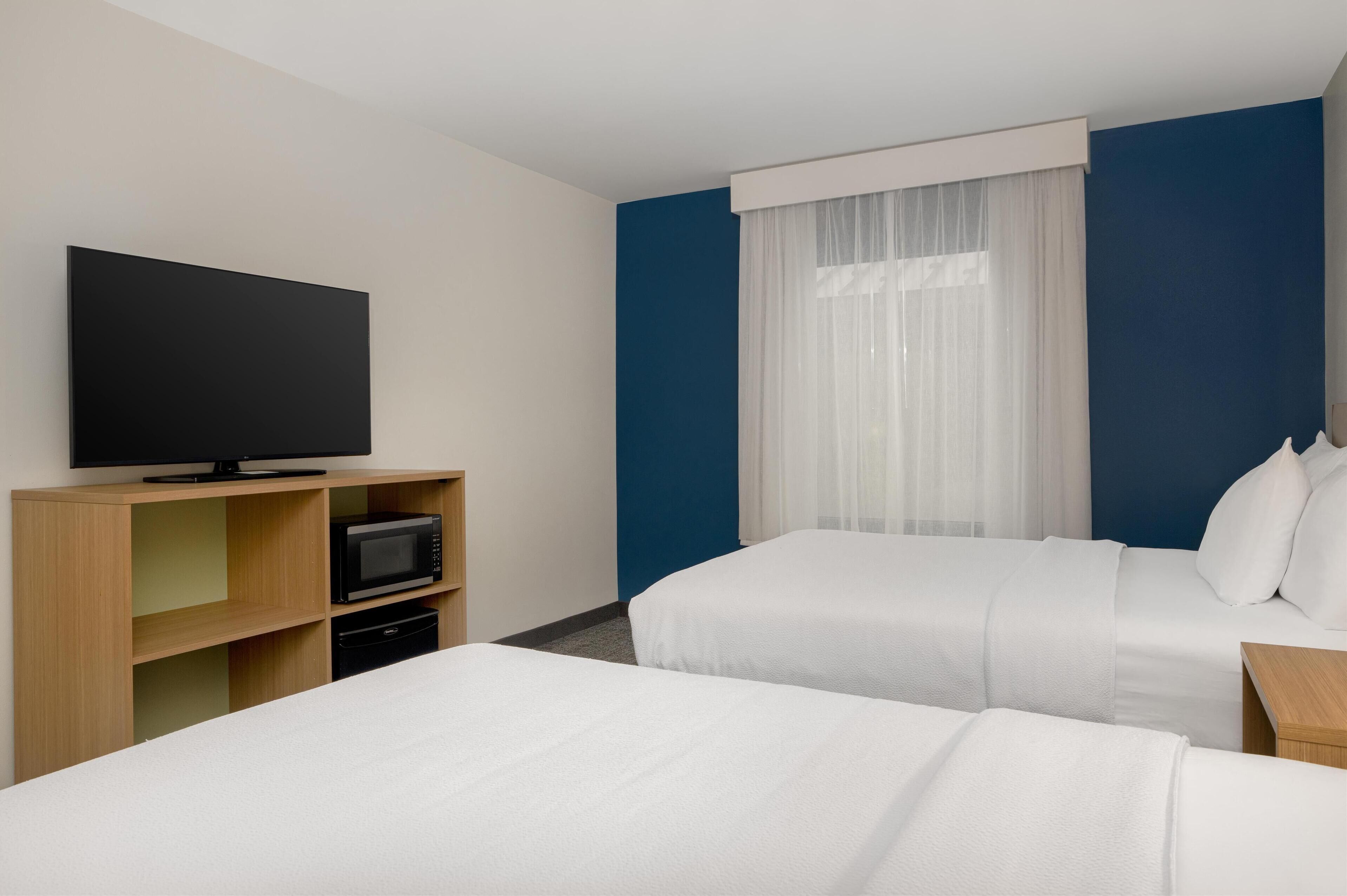 Une chambre d’hôtel avec deux lits, un téléviseur à écran plat, un four à micro-ondes et un petit meuble en bois.