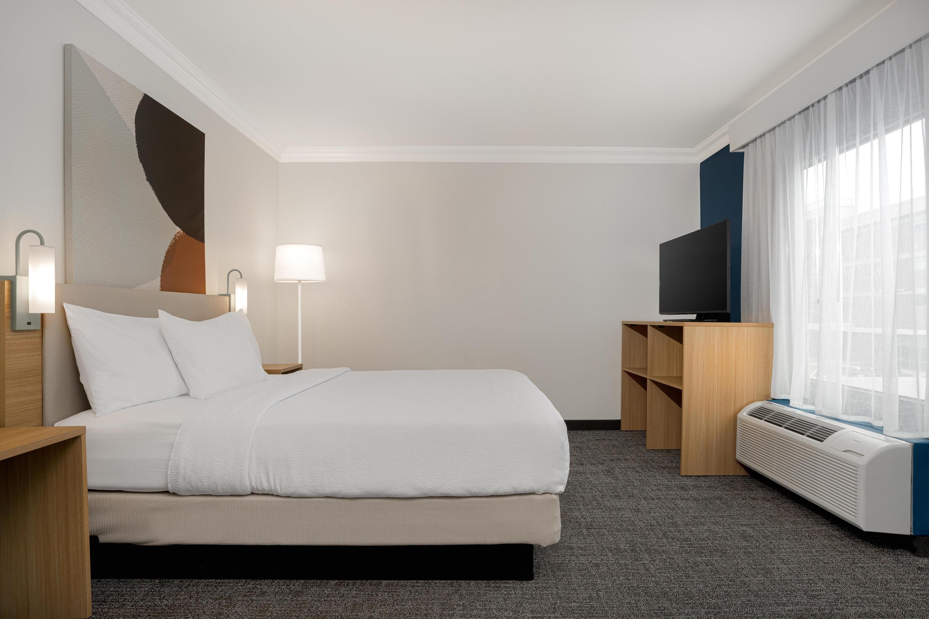 A hotel room with a bed, bedside tables, a lamp, a TV, and a heater.