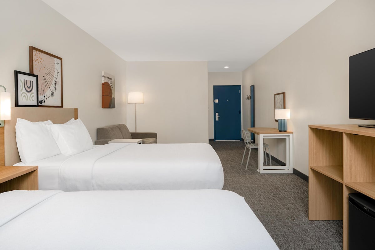 Ett hotellrum med två sängar, ett skrivbord, en stol, en tv och en dörr.