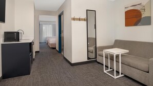 A hotel room with a sofa, a small table, a mirror, a coat rack, and a television on a stand. - Spark by Hilton Rahway (Rahway)