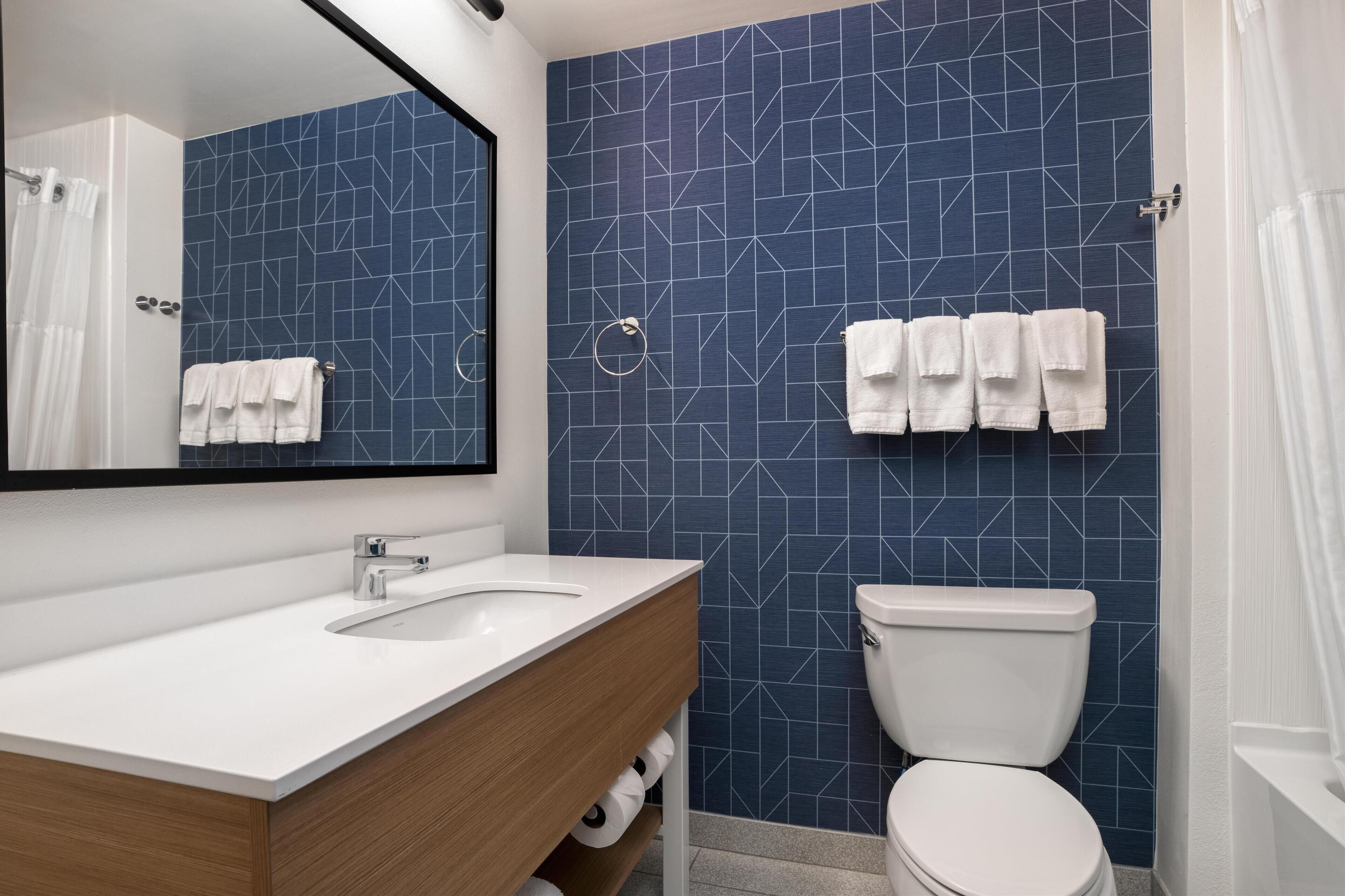 A bathroom with a white sink, a mirror, a toilet, and blue patterned tiles.