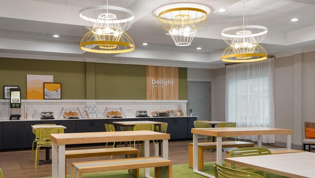 A modern dining area with wooden tables and benches, a kitchen counter with appliances, and a 'Delight in the day' sign on the wall. - Spark by Hilton Rahway (Rahway)