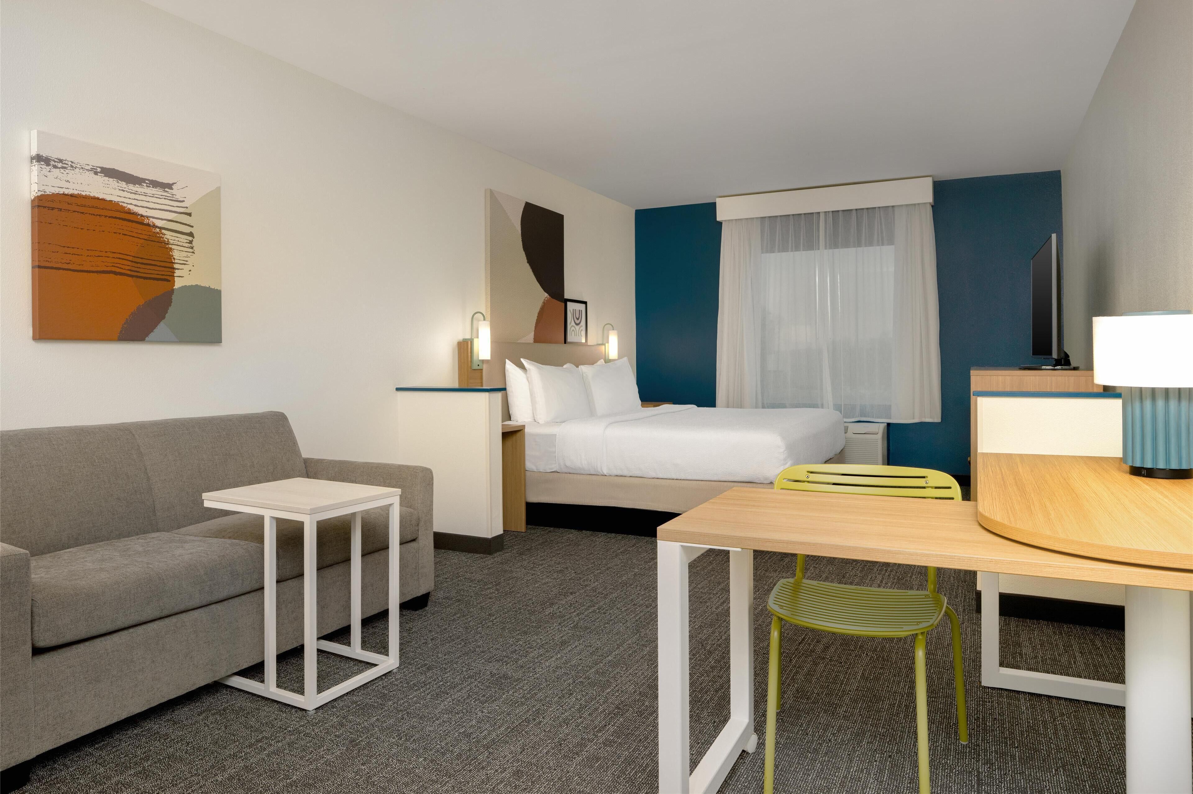 A hotel room with a bed, a sofa, a small table, a chair, and a TV.