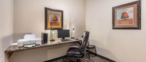 A hotel office with a desktop computer, printer, and two framed pictures on the wall.