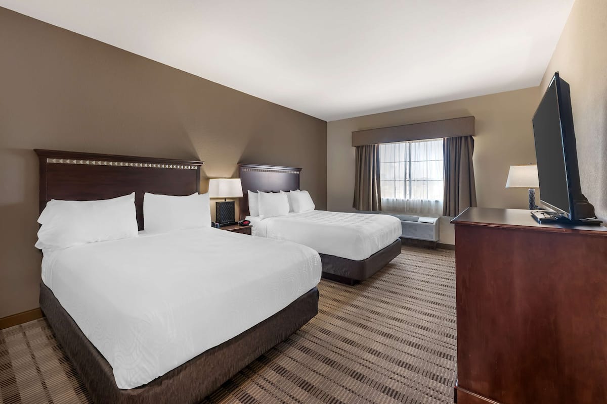 A hotel room with two beds, a television, a desk, and a window with curtains.