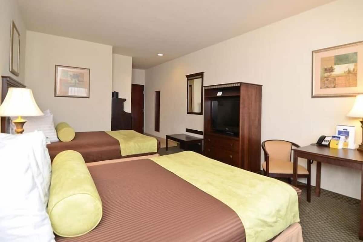 A hotel room with two beds, a desk, a chair, a television, and a mirror.
