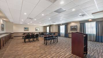 A conference room with a carpeted floor, multiple tables, chairs, a podium, and framed pictures on the walls.