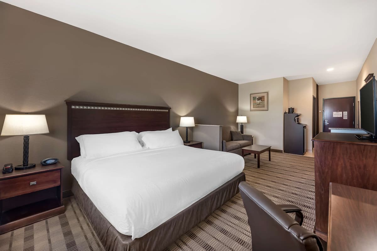 A hotel room with a large bed, two bedside tables with lamps, a desk with a chair, a television, and a small cabinet.
