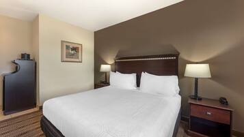 A hotel room with a large bed, two bedside tables with lamps, a dark headboard, a framed picture on the wall, and a small cabinet.