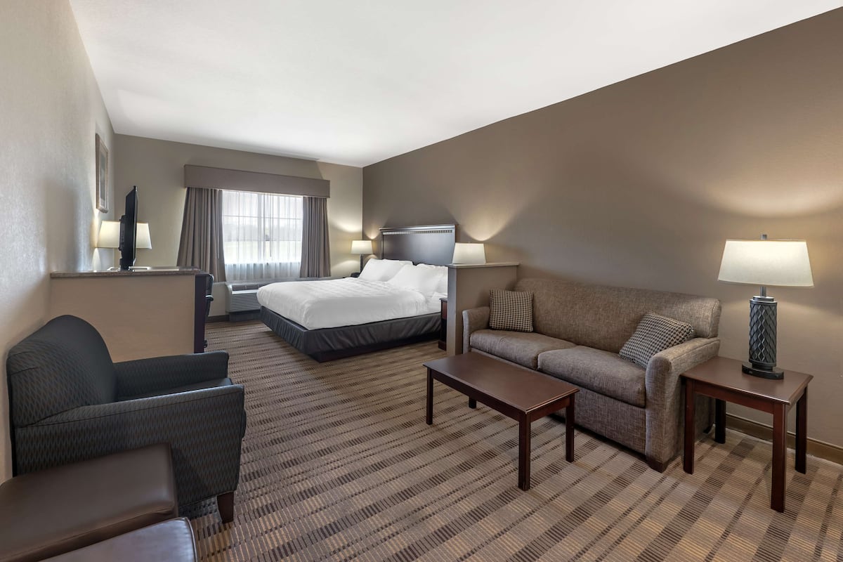 A hotel room with a bed, a sofa, a chair, a coffee table, and a desk with a lamp.
