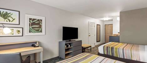 Habitación de hotel con cama, escritorio, televisor y obras de arte en la pared.
