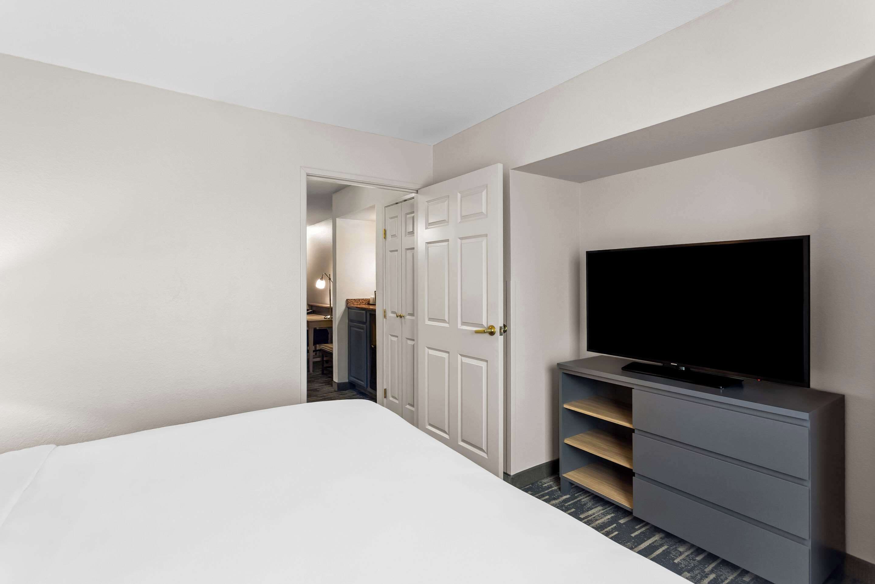 Une chambre d’hôtel avec un lit, un téléviseur posé sur un meuble, une armoire et une porte donnant sur un couloir.