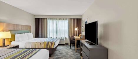 A hotel room with two beds, a desk, a television, and a window with curtains.