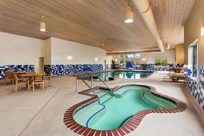 An indoor swimming pool with a unique design, surrounded by wooden furniture and a tiled wall. - Country Inn & Suites by Radisson, Portage, IN (Portage)