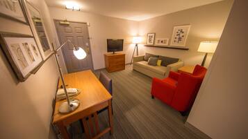 A hotel room with a wooden desk, a television, a sofa, and a red chair.