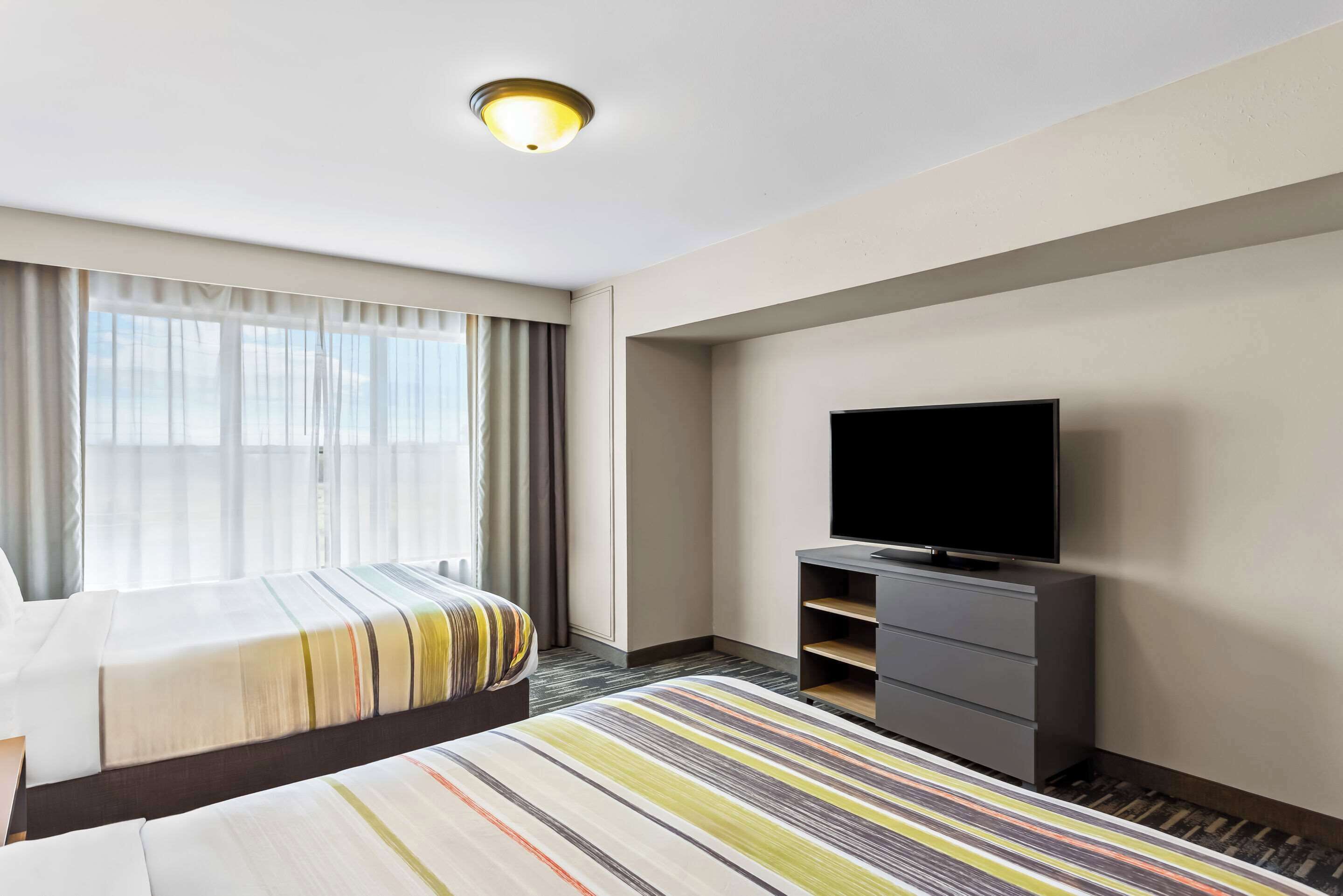A hotel room with two beds, a television on a stand, and a large window with curtains.