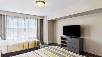 A hotel room with two beds, a television on a stand, and a large window with curtains.