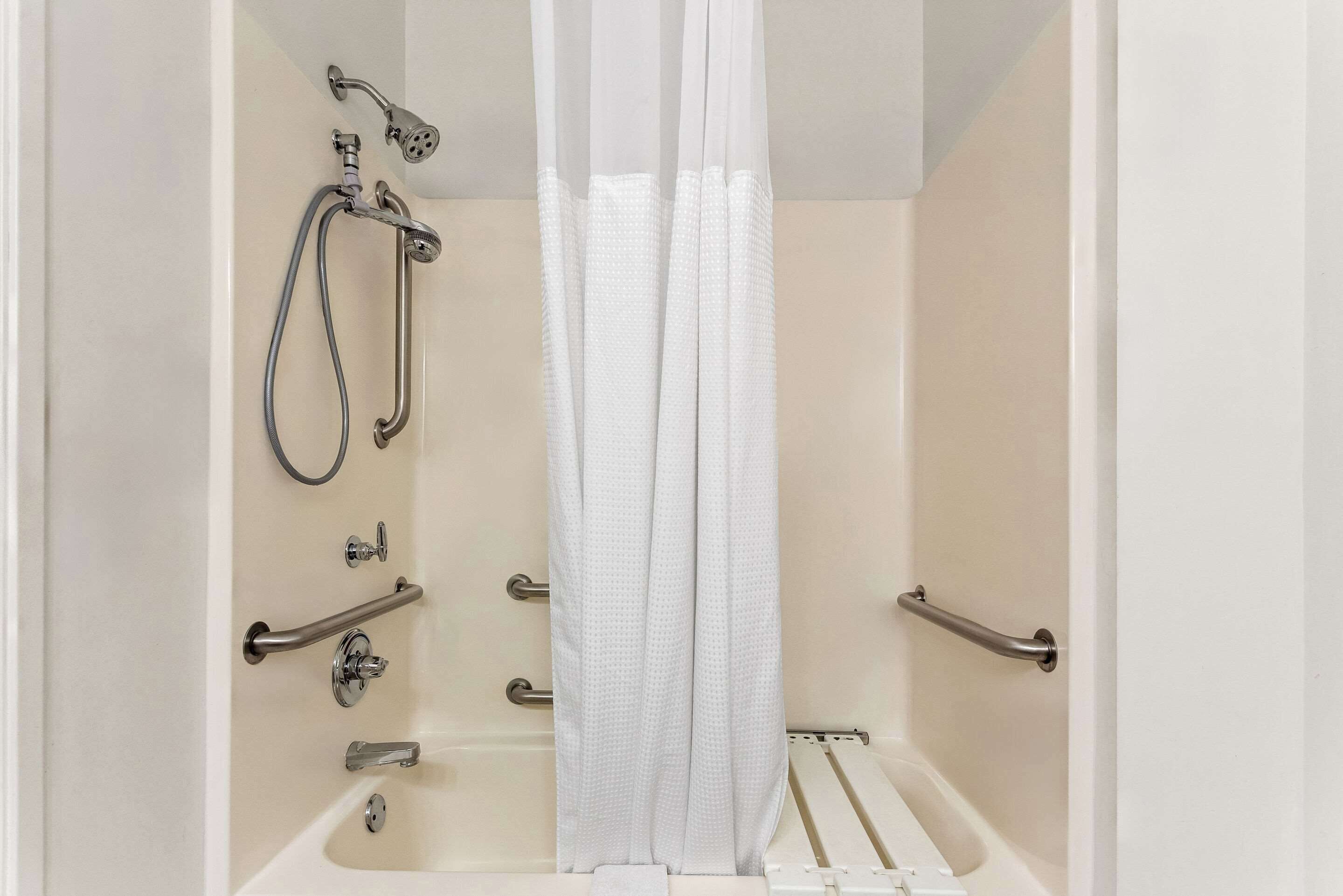 A bathroom with a bathtub, shower, and handrails.