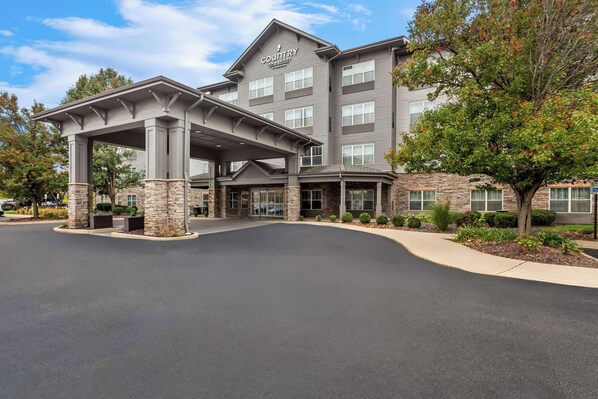 A multi-story hotel with a covered entrance, stone pillars, and a landscaped driveway. - Country Inn & Suites by Radisson, Portage, IN (Portage)