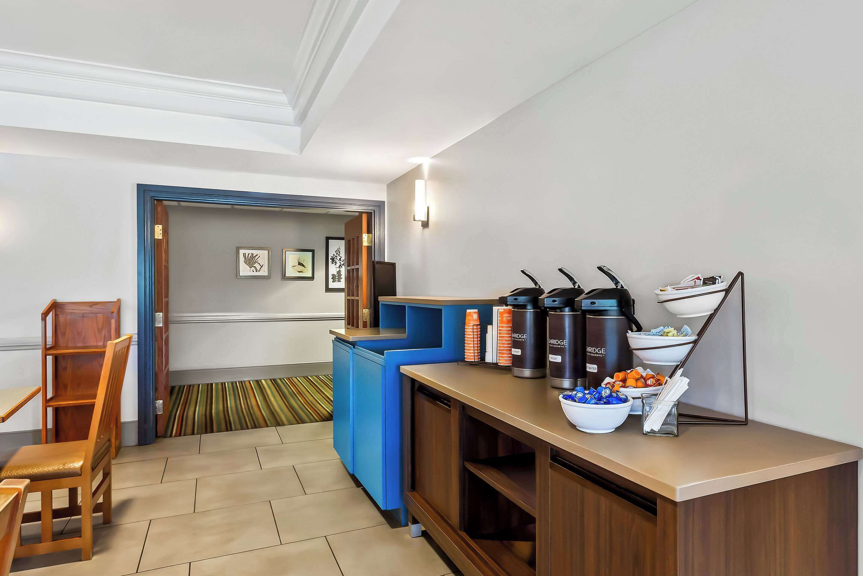 Un espace d’accueil d’hôtel comprenant un comptoir, des machines à café et un bol rempli de collations.