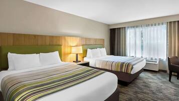 A hotel room with two beds, a green headboard, a lamp, a chair, and a large window with curtains.