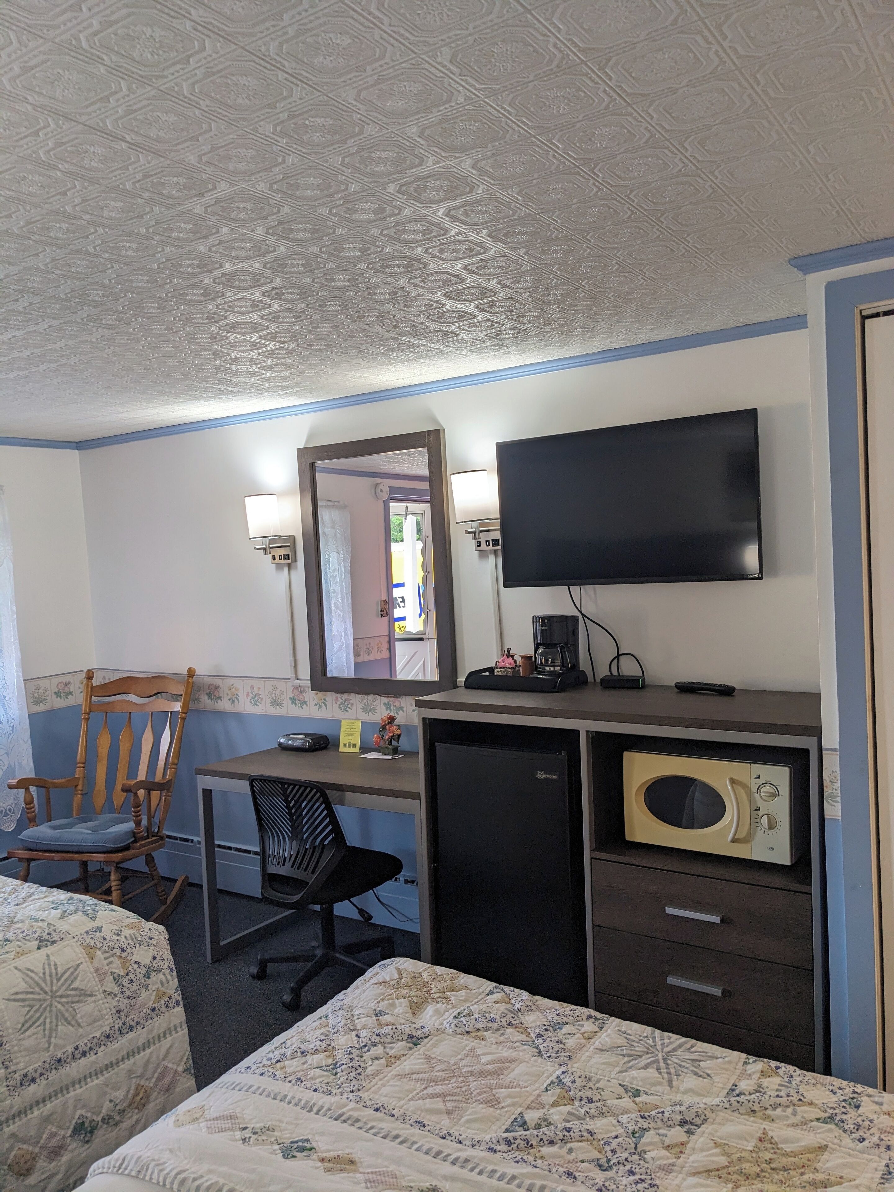 A hotel room with a bed, a desk with a computer, a television, a microwave, and a chair.