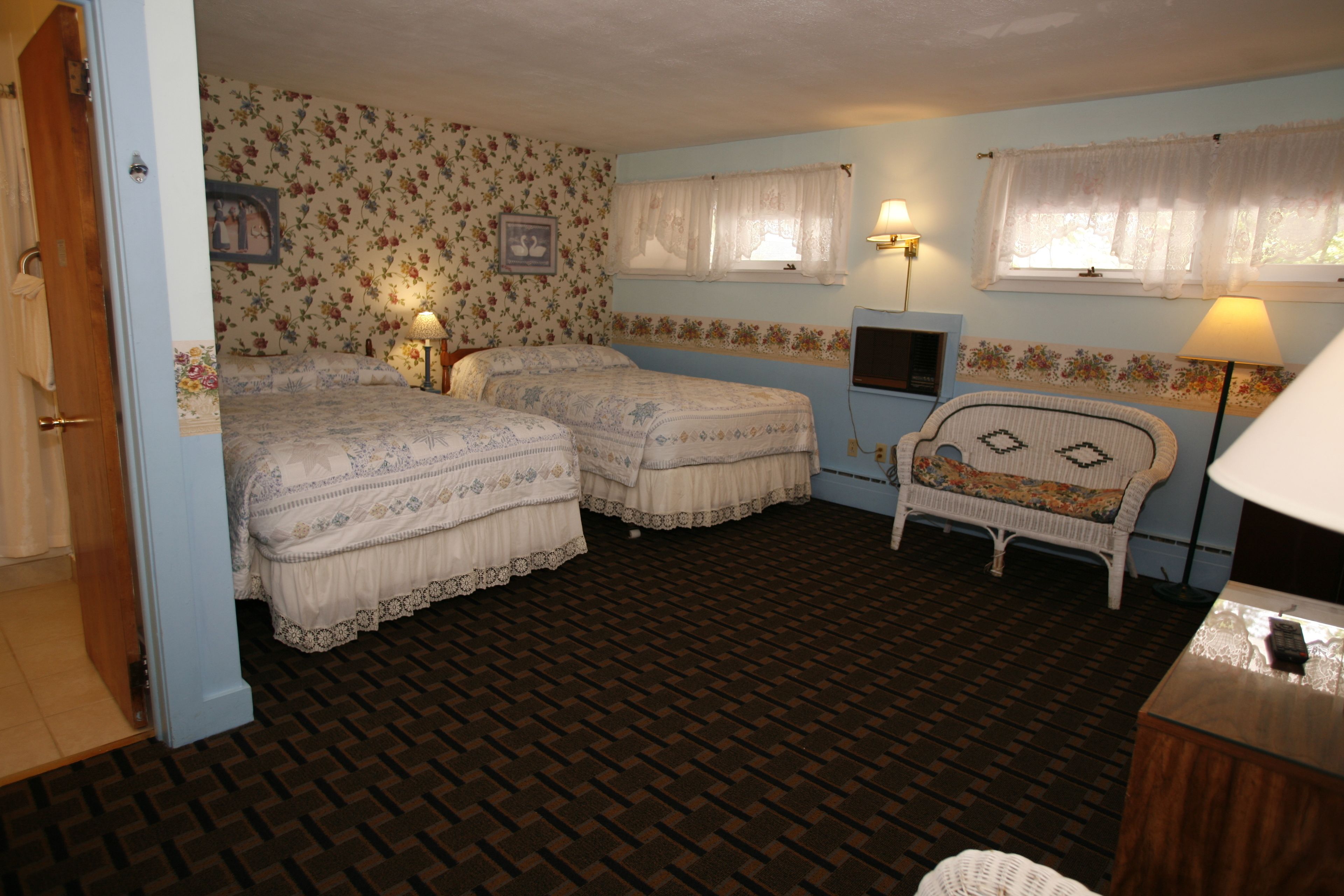 Quarto com duas camas, uma cadeira, televisão e abajur.
