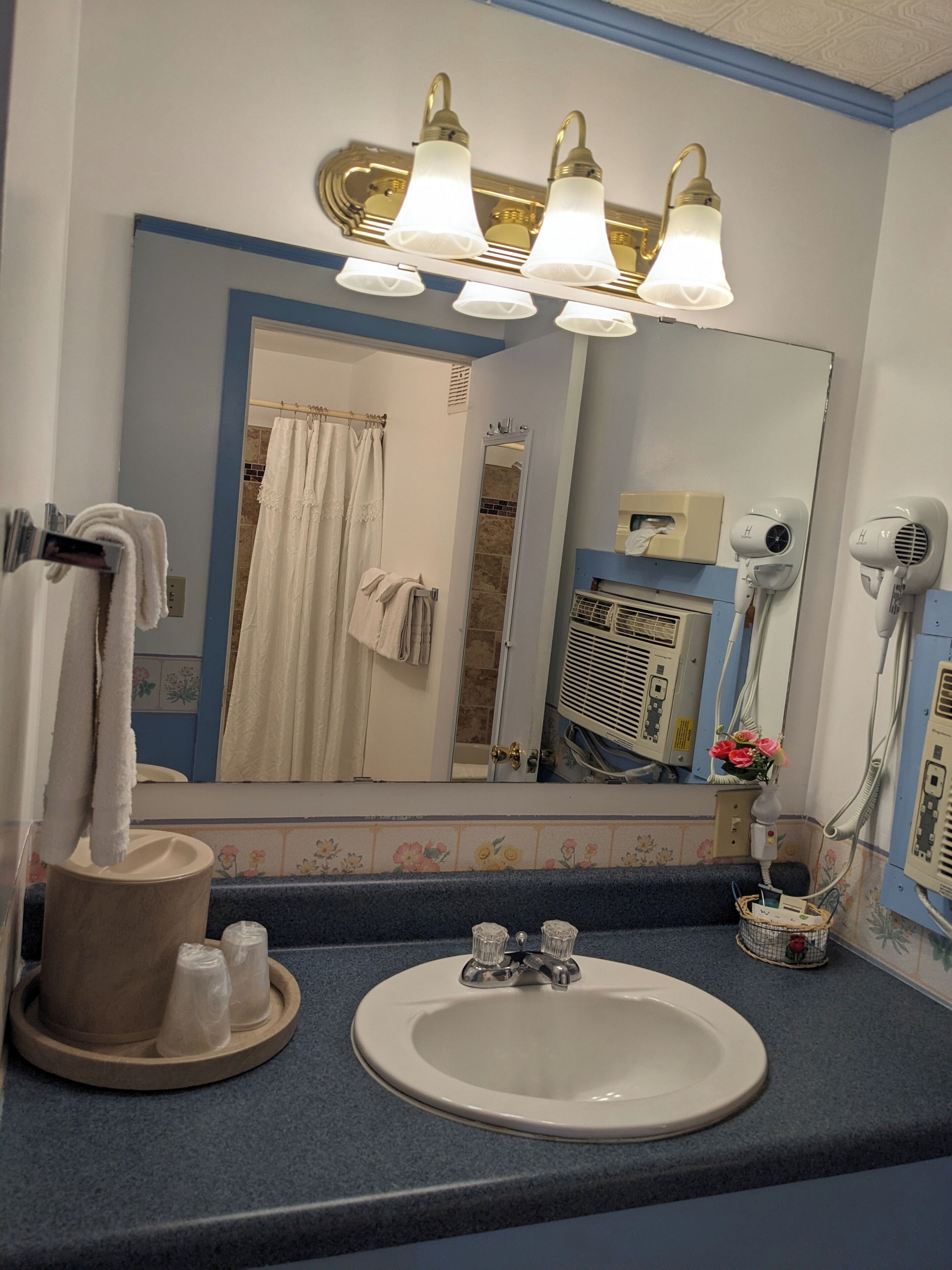 A bathroom with a sink, mirror, towel rack, and hair dryers.