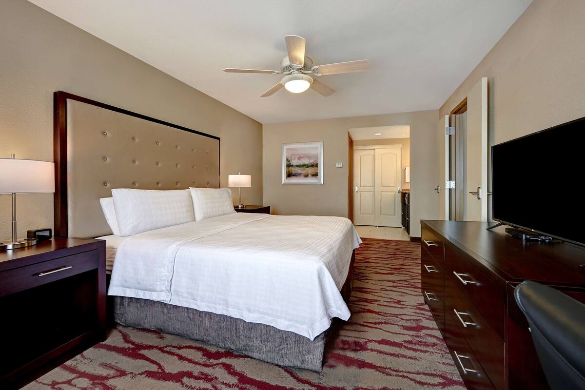 Une chambre d’hôtel avec un grand lit, un ventilateur de plafond, une télévision, une commode et un sol recouvert de moquette.
