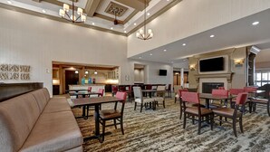 A hotel lobby with a large sofa, dining tables with chairs, a fireplace, and a television mounted on the wall.