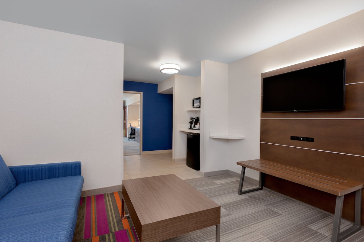 A modern living room with a blue sofa, a wooden coffee table, and a flat-screen TV mounted on the wall.