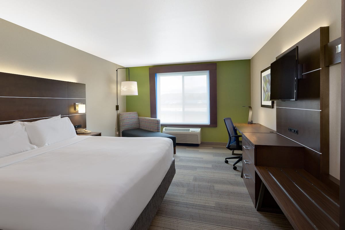 A hotel room with a large bed, a desk, a chair, a television, and a window.