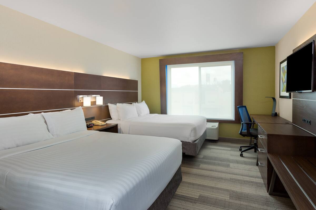 A hotel room with two beds, a desk, a chair, a TV, and a window.