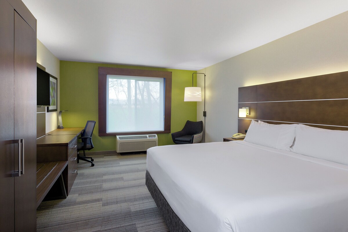 A hotel room with a bed, desk, chair, and a large window.