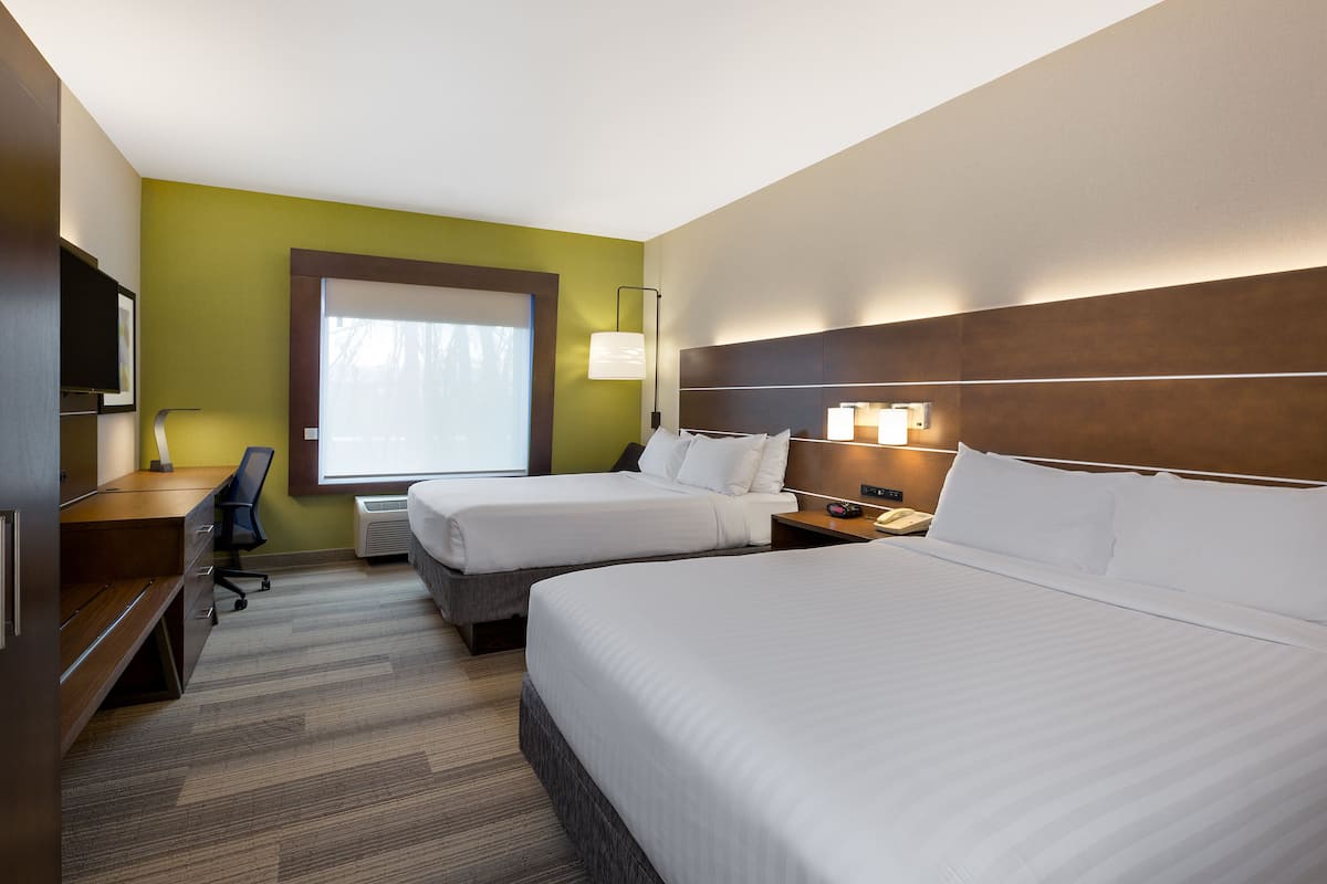 A hotel room with two beds, a desk, a chair, and a TV.