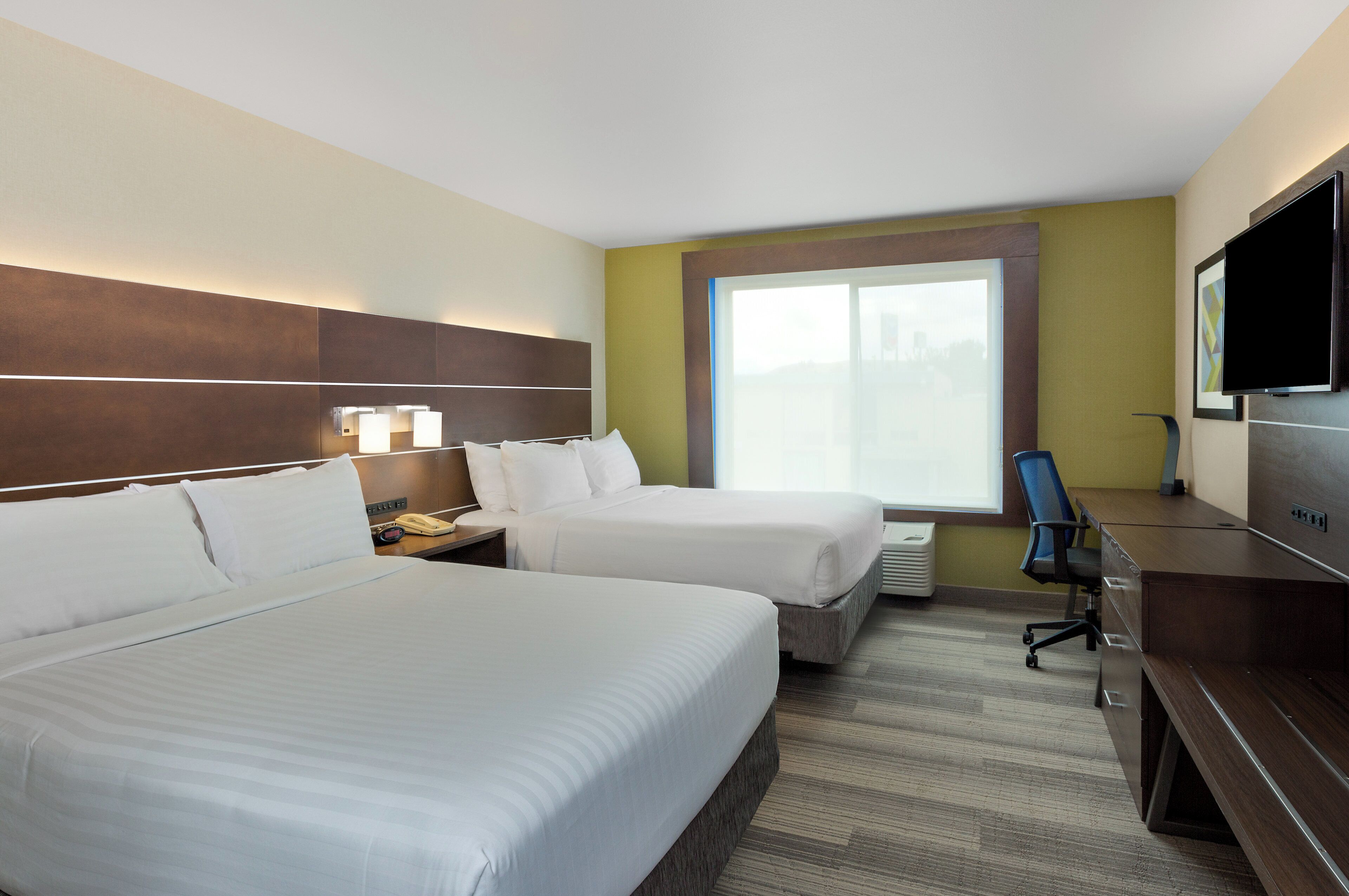 A hotel room with two beds, a desk, a chair, a TV, and a window with a view.