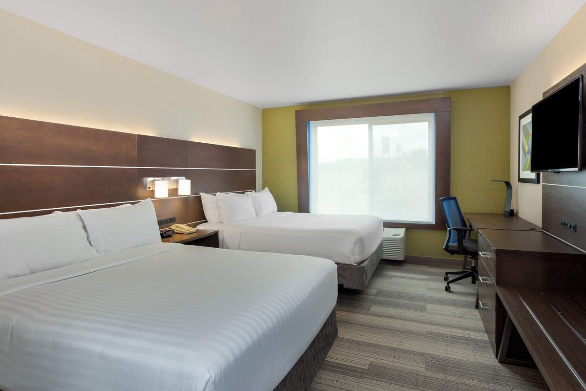 A hotel room with two beds, a desk, a chair, a TV, and a window.