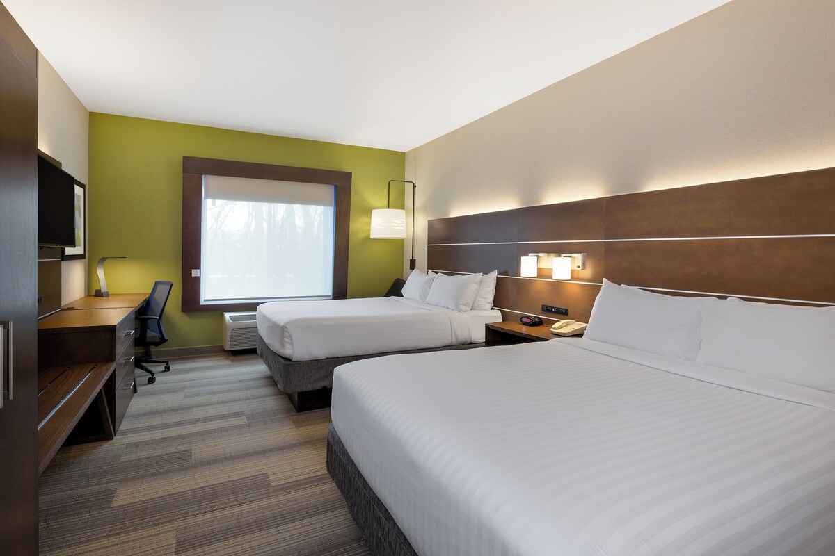 A hotel room with two beds, a desk, a chair, and a TV.