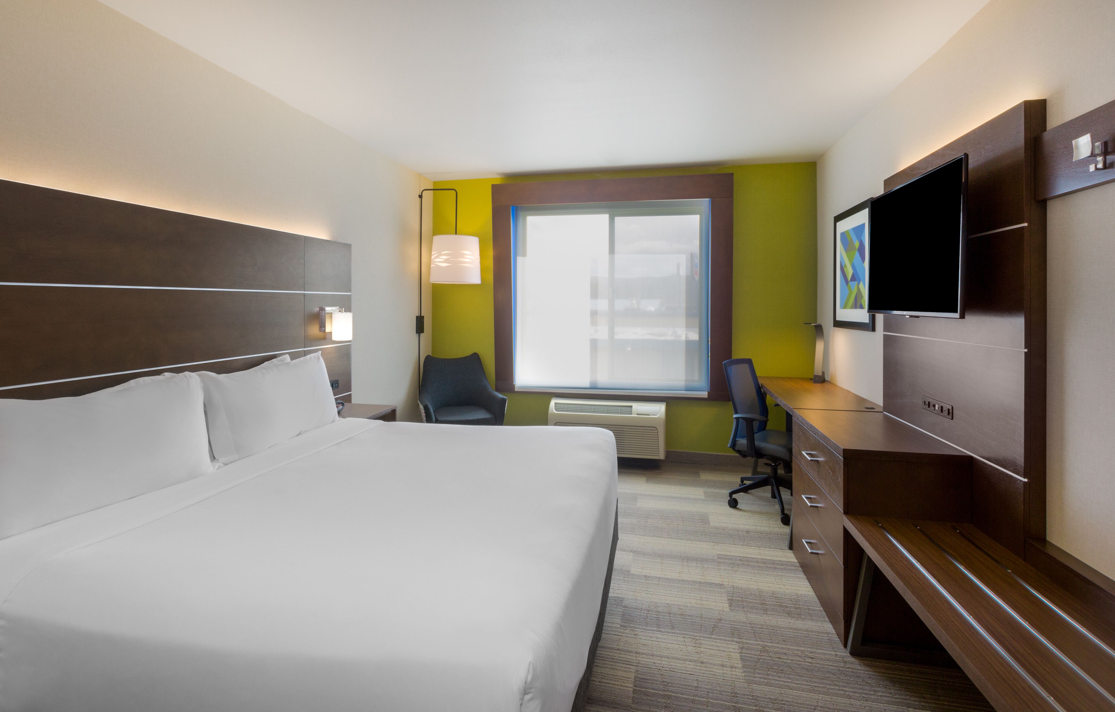 A hotel room with a large bed, a desk, a chair, a TV, and a window with blinds.