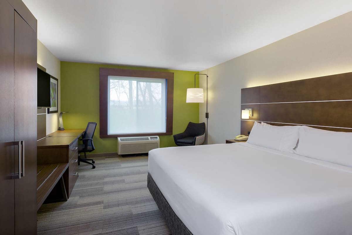 A hotel room with a bed, desk, chair, and a large window.