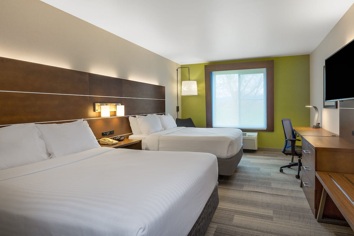 A hotel room with two beds, a desk, a chair, a TV, and a window with natural light.