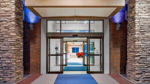 A hotel entrance with a stone facade, a glass door entrance, and a blue carpet leading inside.