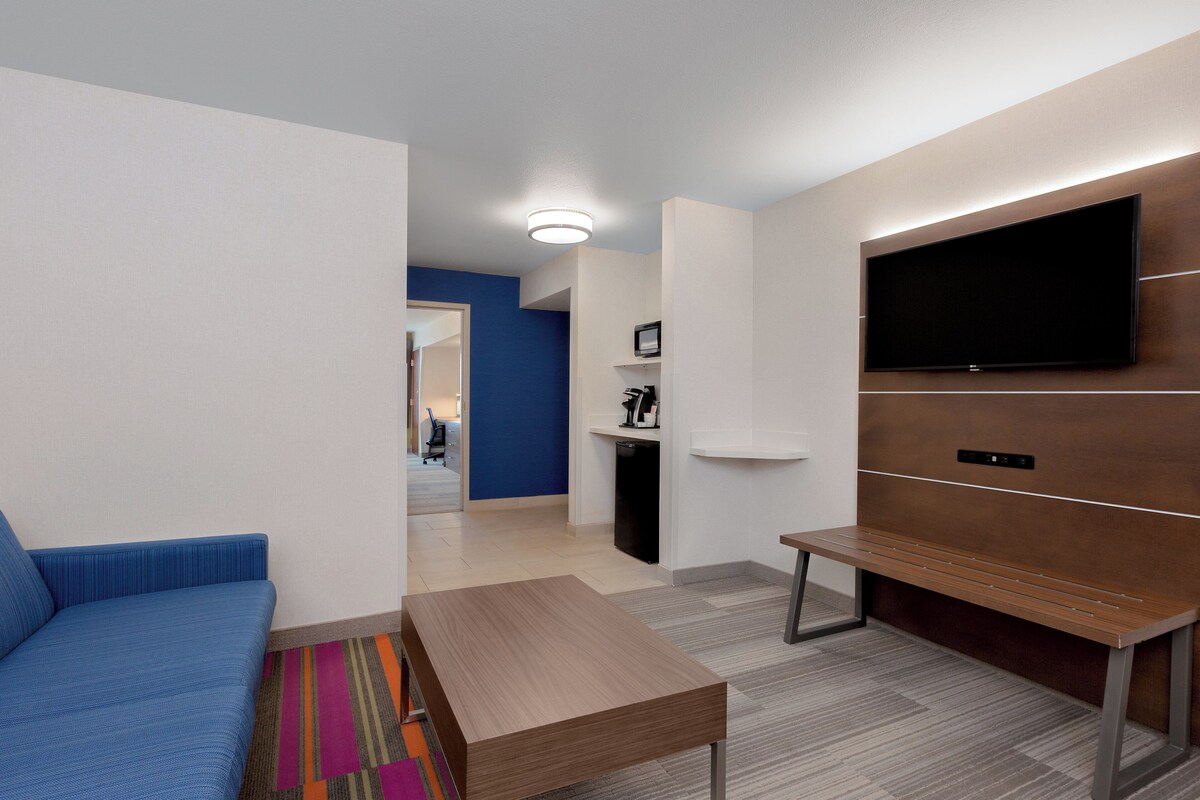 A modern living room with a blue sofa, a wooden coffee table, and a flat-screen TV mounted on the wall.