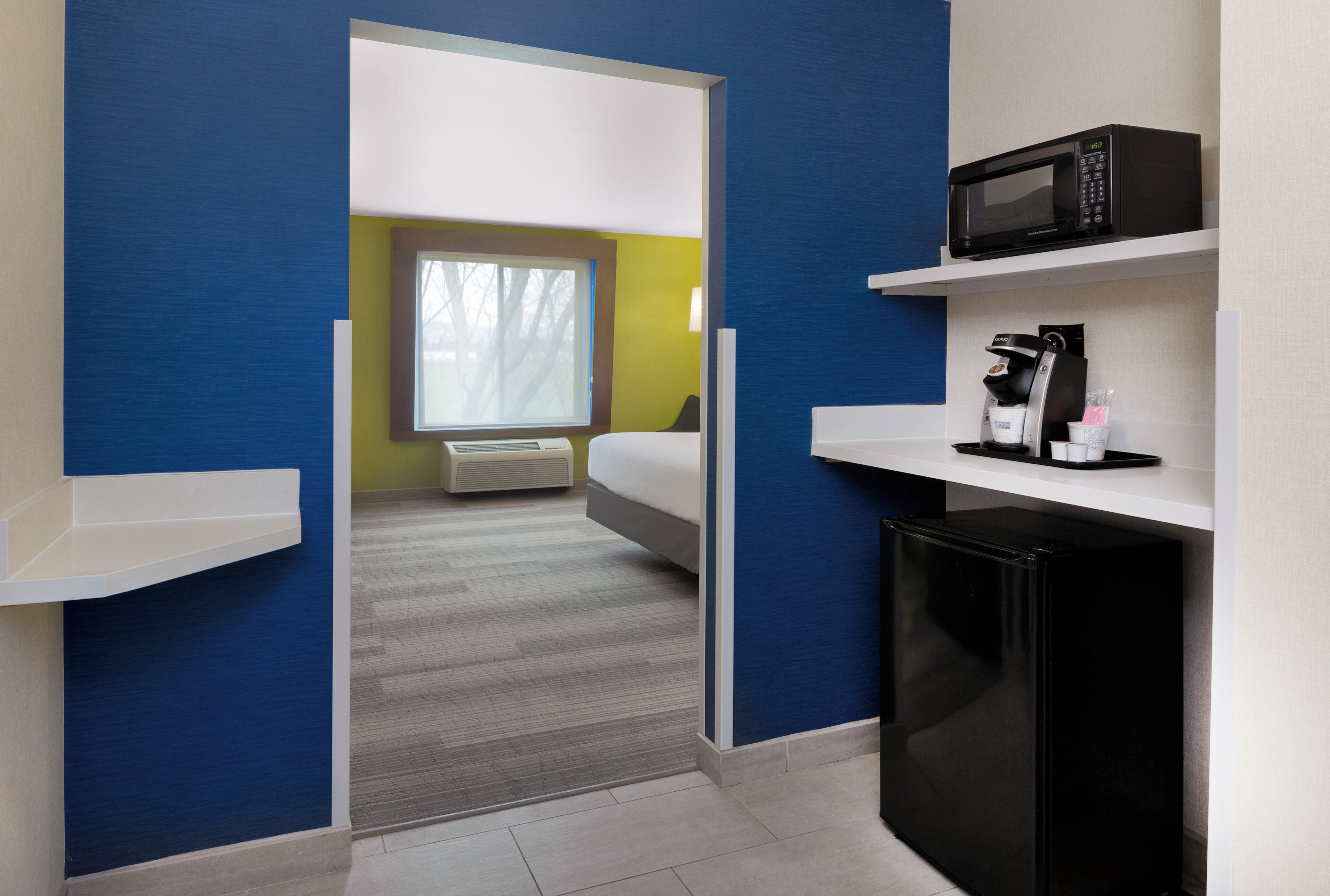 A hotel room with a bed, a microwave, a coffee machine, and a small refrigerator.